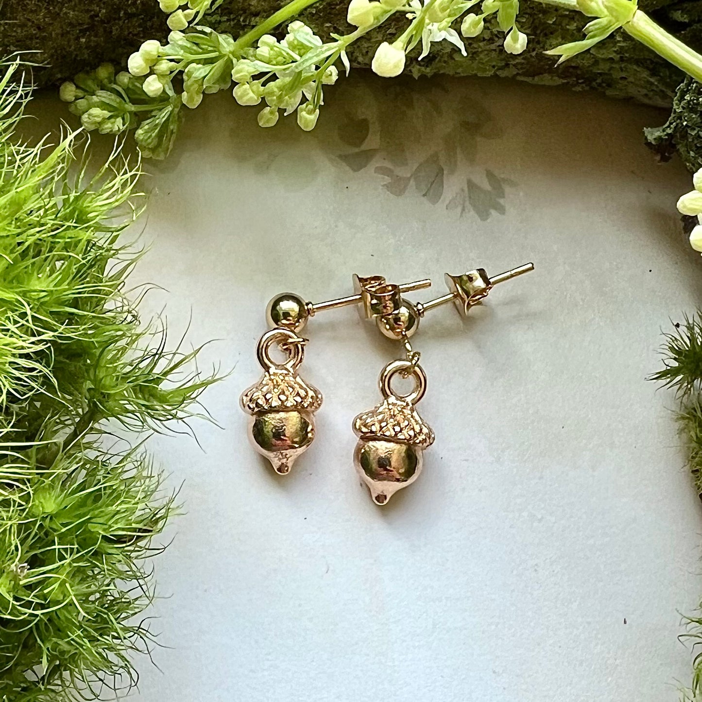 Keltiska örhängen med små, guldfärgade ekollon i rostfritt stål